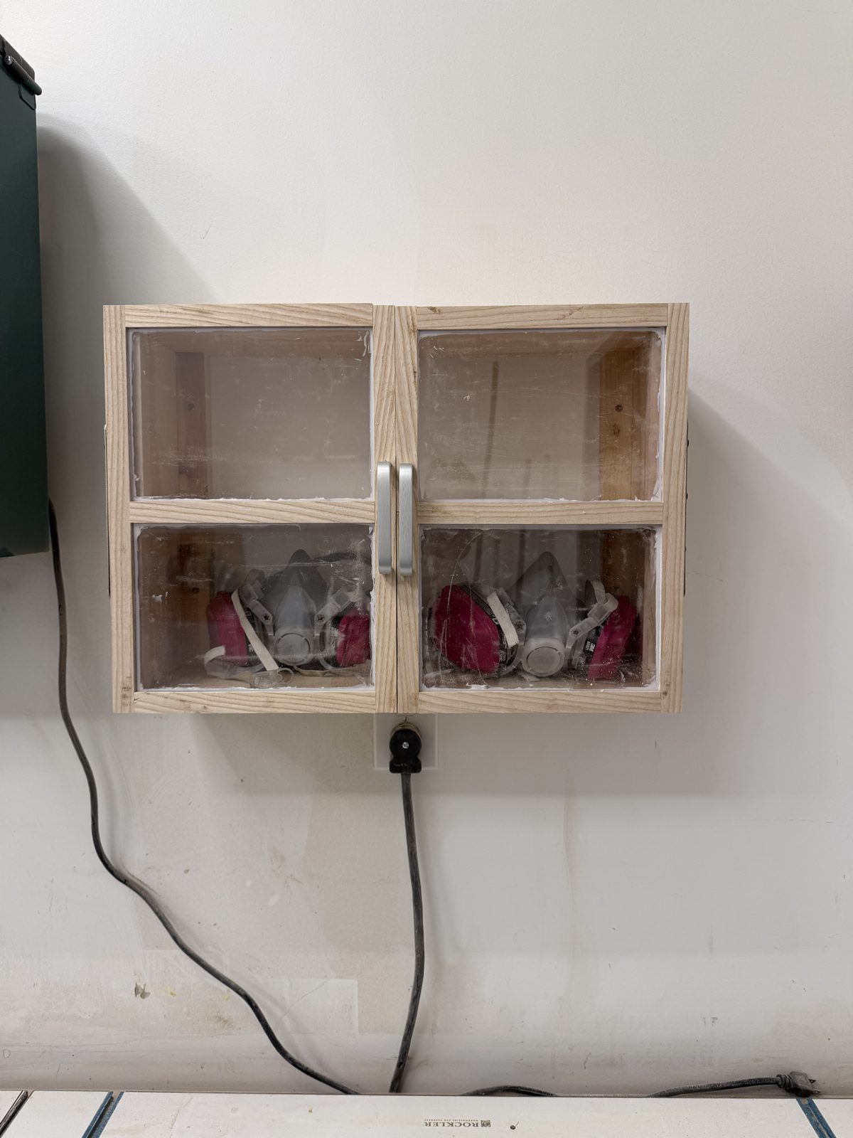 Finished wall cabinet with wood-framed acrylic doors holding two respirators