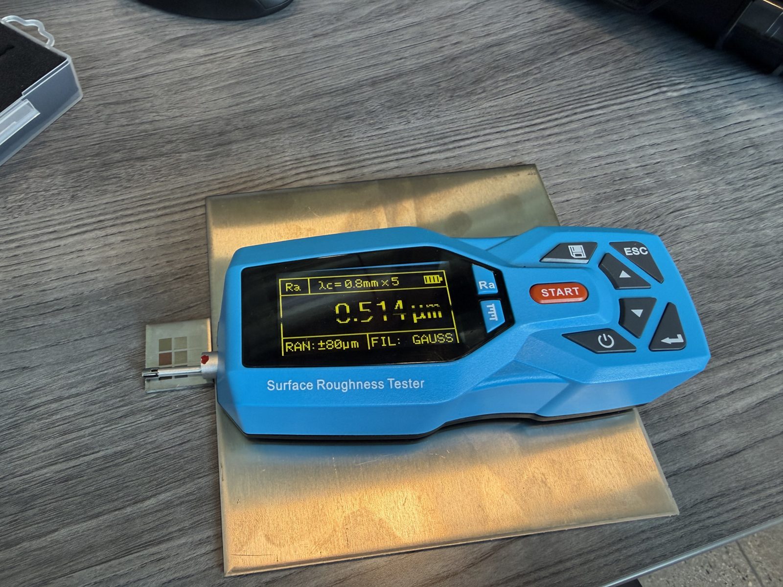 Handheld roughness tester resting on a metal coupon