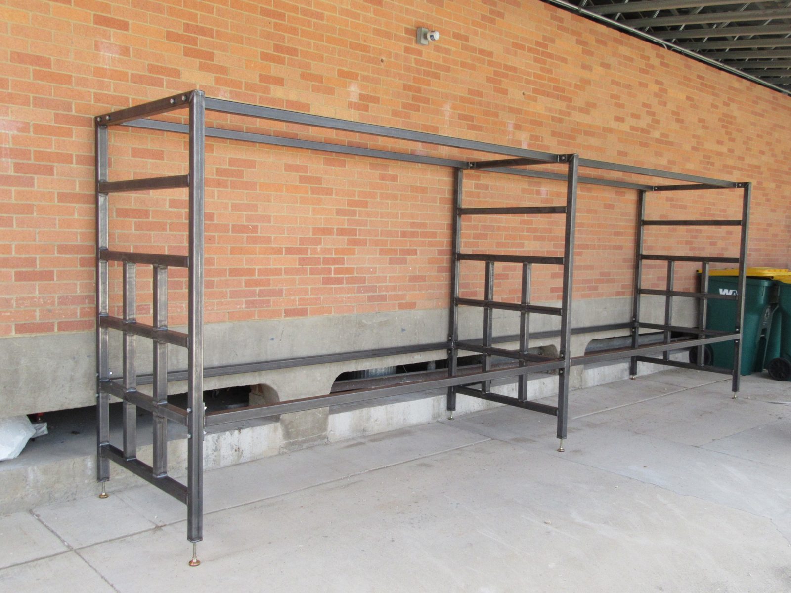 Finished steel storage rack with bolted square-tube frames and leveling feet, standing against a brick wall