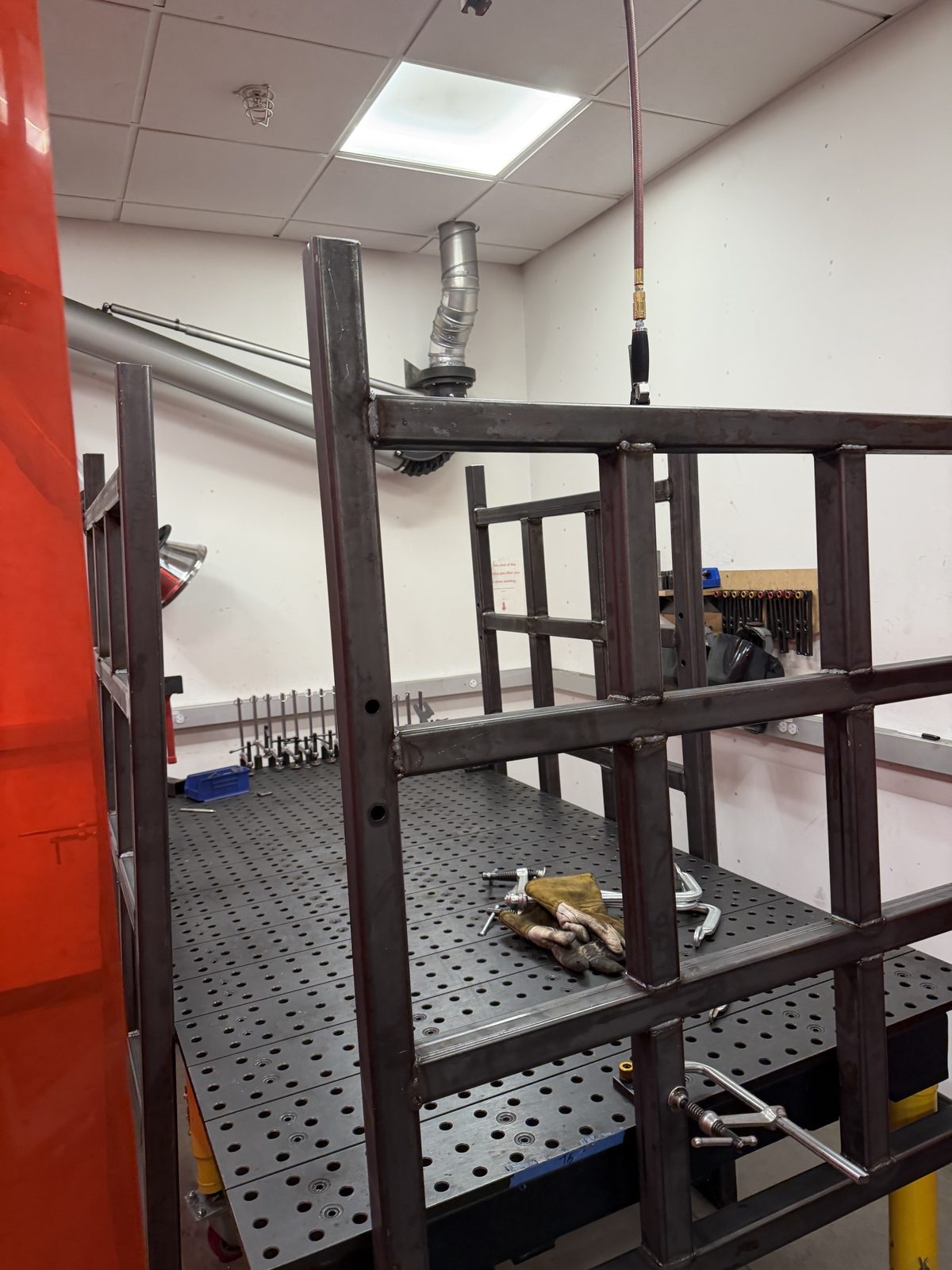 A welded square-tube end frame clamped on the welding fixture table