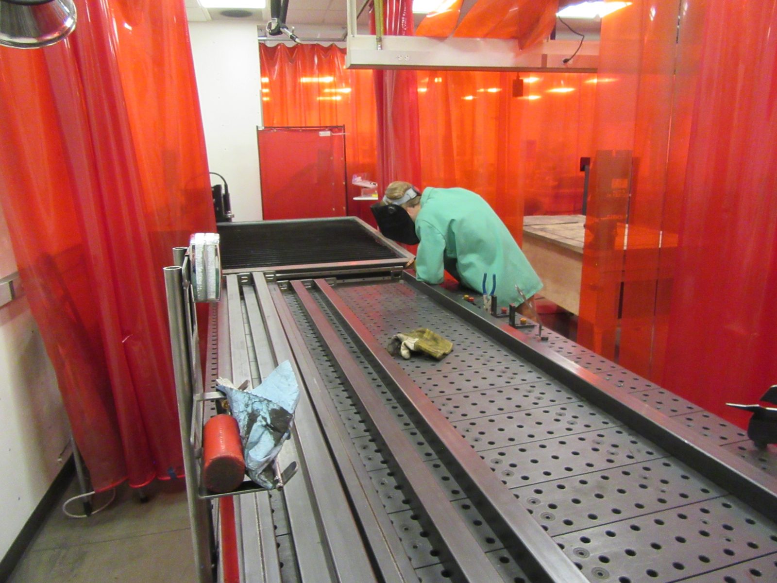 The rack's long rails on the fixture table inside the welding booth during fabrication